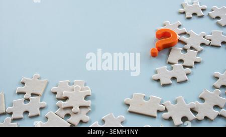 An orange question mark symbol placed over a messy cluster of white puzzle pieces with negative space on a blue background Stock Photo