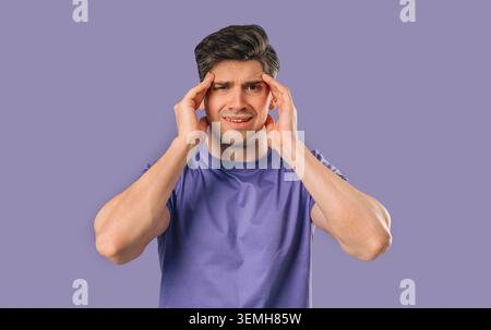 30s aged man having headache, touching temples, Suffering on violet background. Stock Photo
