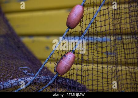A single orange fishing float is framed by weathered netting in a close maritime detail scene from Helgoland. Stock Photo