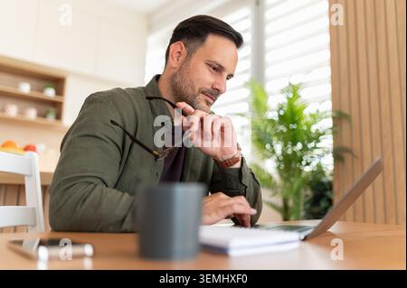 Man working remotely with laptop at home, focusing on tasks and managing business with modern technology, engaging in online education, distance learn Stock Photo