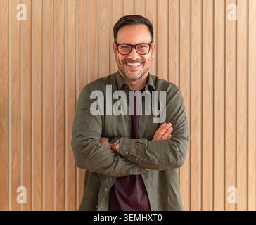 Mature man smiling, standing with arms crossed, wearing glasses and casual clothing, feeling confident and successful in a professional or business en Stock Photo