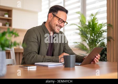 Smiling man with glasses working from home, using his laptop for an online meeting or video call, showing remote work flexibility and professional com Stock Photo