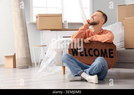 Thoughtful young man with doormat sitting in room on moving day Stock Photo