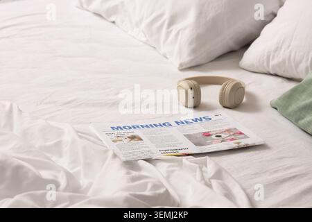 Headphones with newspaper on unmade bed in hotel room Stock Photo