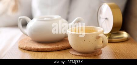 Cozy morning tea still life with white teapot and ceramic cup on wooden table beside clock in soft natural light Stock Photo