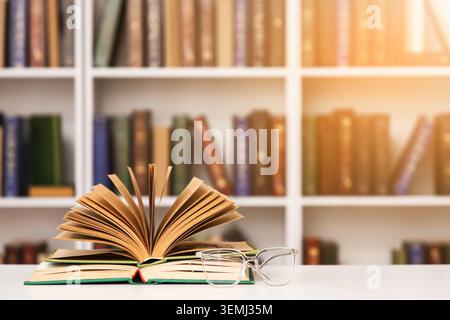 Open book stacked on textbooks with eyeglasses on table in library, warm sunlight, education and reading concept Stock Photo