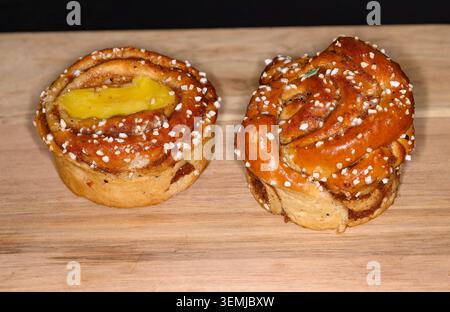 Two cinnamon rolls sit on a wooden board in a kitchen. One roll features pastry cream on top, while the other has a traditional swirl. The setting is Stock Photo