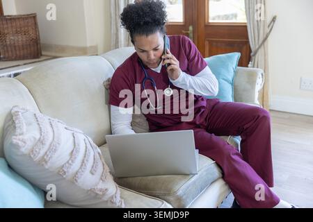 Silver laptop and smartphone are sitting on beige sofa near stethoscope and pillows Stock Photo