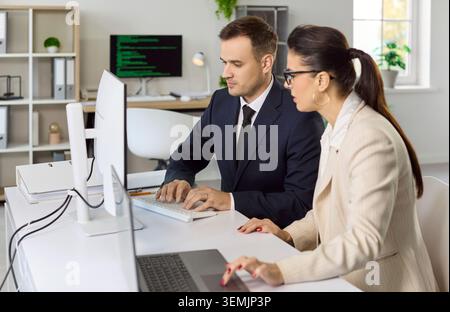 Colleagues collaborating at desktop computers in modern office, coding tasks Stock Photo