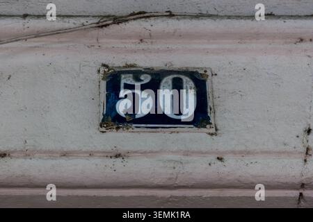 A chipped and worn dark blue enamel house number 50 plaque with white numerals set into a weathered painted rendered wall in a French village Stock Photo