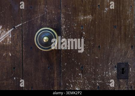 A brass door bell button and keyhole on a heavily weathered and scratched dark wooden door in a French village Stock Photo