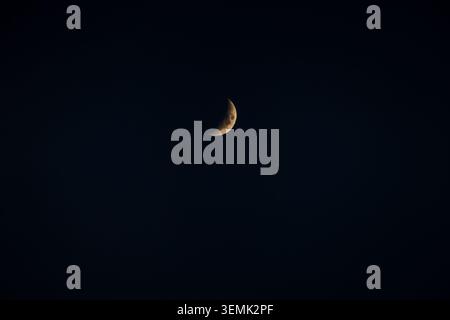 A glowing golden crescent moon hangs against a deep dark blue-black night sky, creating a minimal and serene celestial scene Stock Photo
