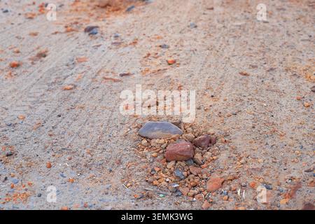 Small stones and orange clay fragments lie scattered on a dry sandy road surface. Sandy texture view of an unpaved rural dirt pathway ground with tyre Stock Photo