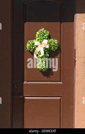 Decorative cross-shaped greenery wreath with ribbon mounted on a residential front door Stock Photo