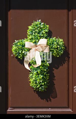 Decorative cross-shaped greenery wreath with ribbon mounted on a residential front door Stock Photo