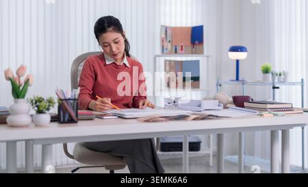 Asian woman designer sketching furniture layout blueprint at modern workspace desk with organized creative studio Stock Photo