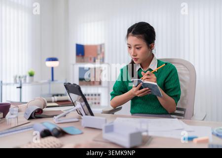 Young Asian women furniture designer writing notes planning creative project working with tablet at home office Stock Photo