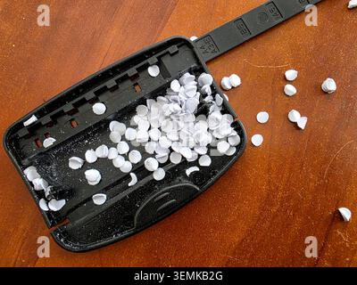 A hole punch tool is open and shows white paper circles spilled on a wooden surface. The tool was just used for making holes in sheets of paper. Stock Photo