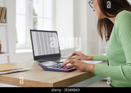 Female accountant using calculator and laptop for financial audit in bright office Stock Photo