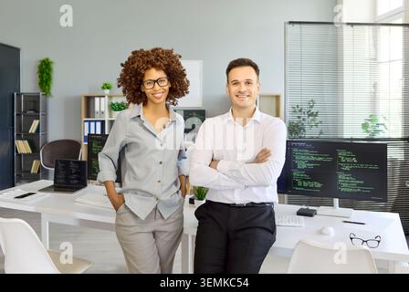 Smiling programmers and developers in modern office, teamwork with coding monitors Stock Photo