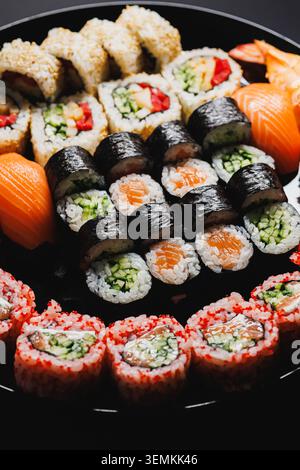 Different types of sushi are arranged neatly on a black plate. The platter includes salmon, cucumber rolls, and rice. This dish is common in Japanese Stock Photo