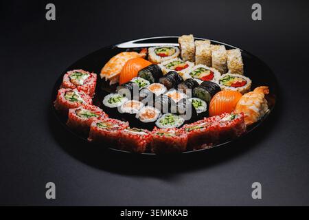Sushi rolls and sashimi are arranged on a black plate. The plate contains different types of sushi, including maki and nigiri, ready for diners in a r Stock Photo