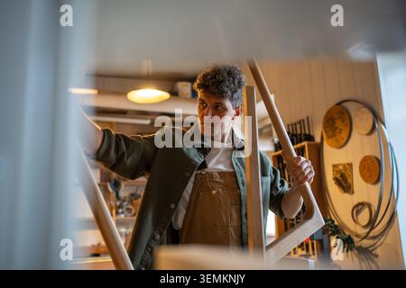 Craftsman inspects table legs and base, ensuring even surfaces and quality construction in workshop Stock Photo
