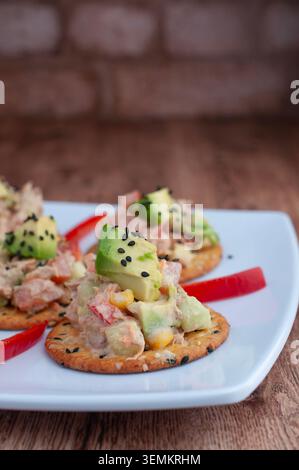 Tuna tapas with cucumber, mayonnaise and avocado with a strip of red pepper, placed on a white plate, with brick walls in the background. Vertical wit Stock Photo