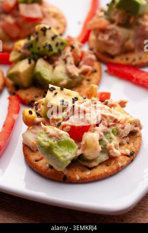 Tuna tapas with cucumber, mayonnaise and avocado with a strip of red pepper, placed on a white plate, with brick walls in the background, vertical clo Stock Photo
