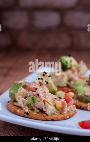 Tuna tapas with cucumber, mayonnaise and avocado with a strip of red pepper, placed on a white plate, with brick walls in the background, avocado on t Stock Photo