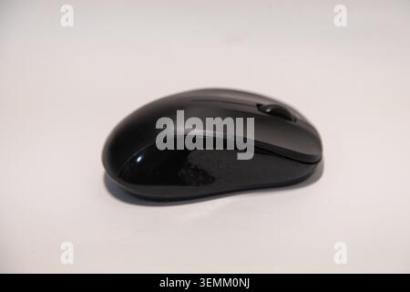 A modern black wireless computer mouse resting on a clean white surface, showcasing its ergonomic design and sleek matte finish, perfect for office wo Stock Photo