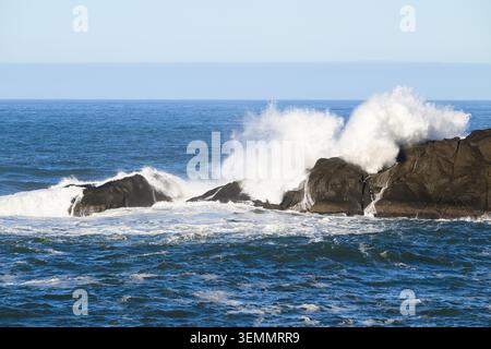 White ocean waves break over coastal rocks with calm sea and horizon Stock Photo