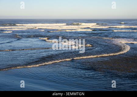 Wave curves into ocean waves breaking on approach to beach with clear horizon Stock Photo