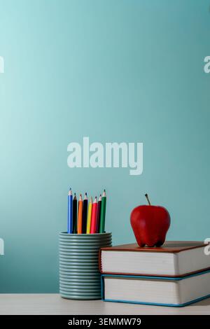 A pencil holder filled with brightly colored pencils next to a red apple on a stack of two books. Education, back-to-school season, creativity Stock Photo