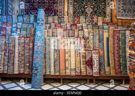 Rolled carpets with intricate geometric and floral patterns fill a traditional shop interior in Fez, creating a colorful textile display. Stock Photo
