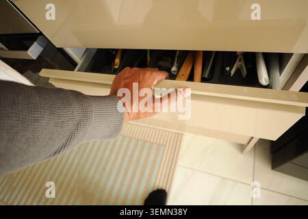 Hand opens drawer with tools in modern kitchen setting Stock Photo