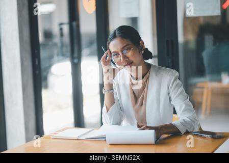 Serious businesswoman thinking with pen at office table, reviewing documents, solving problems and making careful decisions during a focused business Stock Photo