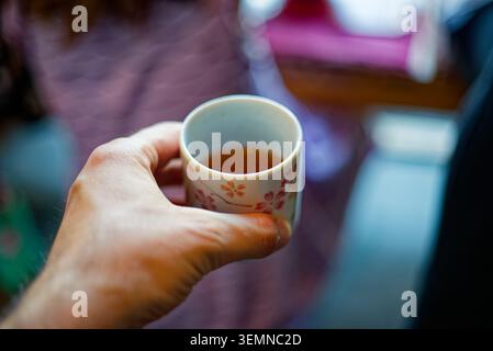 Hand holding a small cup of Japanese tea with soft cafe background and shallow depth of field. Stock Photo
