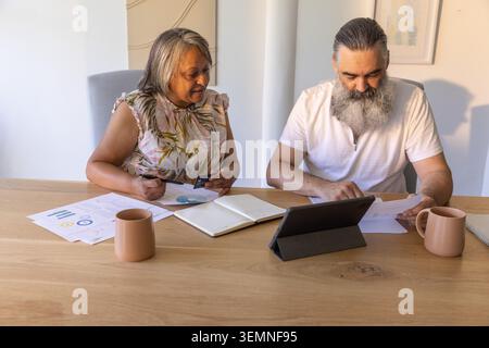 Senior couple sitting at wooden table, examining charts, holding credit card, consulting tablet Stock Photo