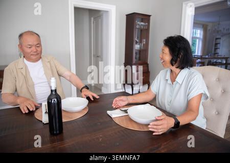 Asian couple with senior woman and mature man sitting at home dining table with dark bottle Stock Photo