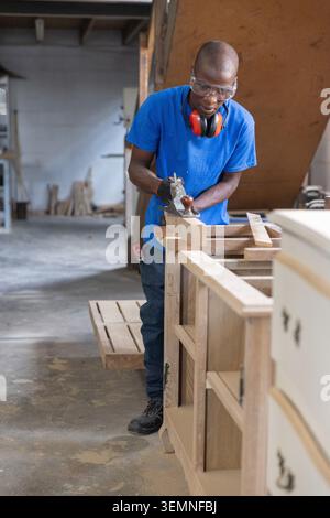 Hand plane smoothing unfinished wooden panel on workbench with scattered sawdust and cabinet frames Stock Photo