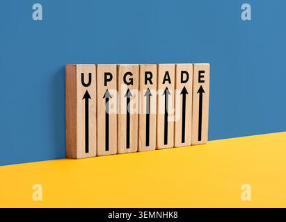 Wooden blocks spelling upgrade with upward arrows symbolize progress, development, and improvement on a yellow and blue background Stock Photo