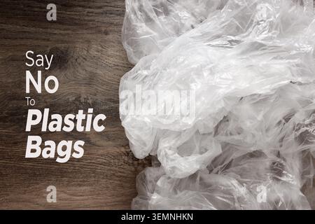 Slogan Say No To Plastic Bags on wooden surface next to crumpled white plastic bags, illustrating environmental awareness Stock Photo