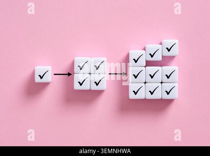 Checkmark cubes illustrating step by step progress, task completion, checklist accomplishment, and growing productivity or performance on a pink surfa Stock Photo