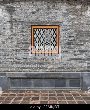 Weathered brick wall with a decorative geometric patterned window and stone base, Imperial City, Hue, Vietnam Stock Photo