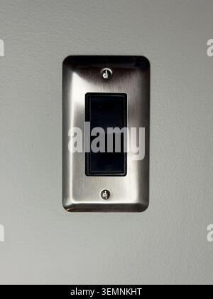 A light switch is fixed to a wall that has a smooth finish. The switch is designed for controlling lighting in the room. It is in a standard location Stock Photo