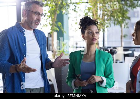 Diverse coworkers meeting in office, African American woman in green blazer holding phone and stylus Stock Photo