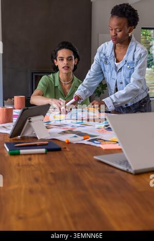 Diverse coworkers collaborating over wooden table in studio, arranging prints and sticky notes. Teamwork, design, planning, brainstorming, creative, w Stock Photo