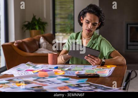 Asian man wearing green shirt studying at home desk holding black tablet and sticky notes Stock Photo