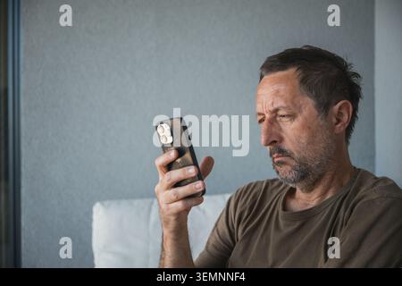 Middle-aged man looking at smartphone with serious expression, selective focus Stock Photo